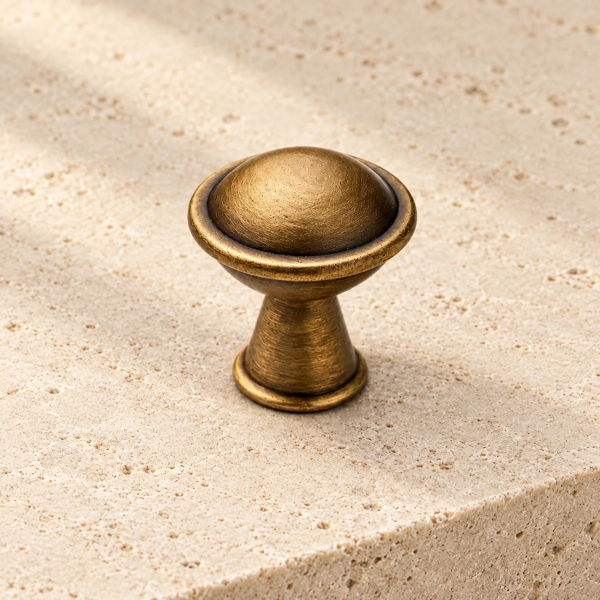 antique brass domed cabinet knob on pale limestone.