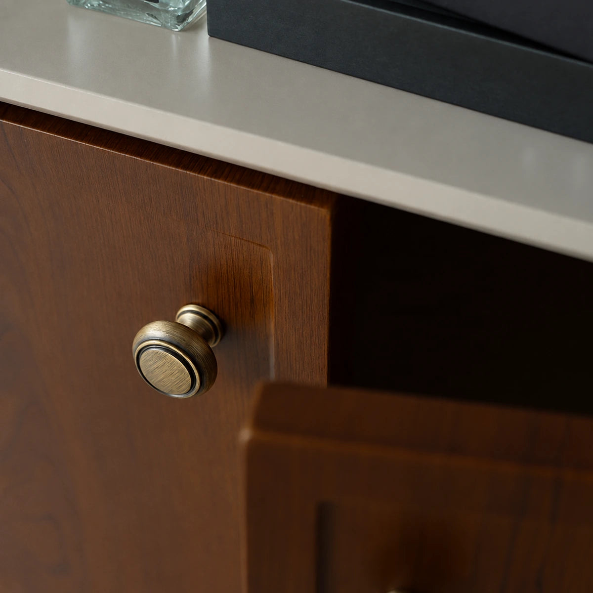 Round antique brass knob with raised ring border installed on a dark wood cabinet