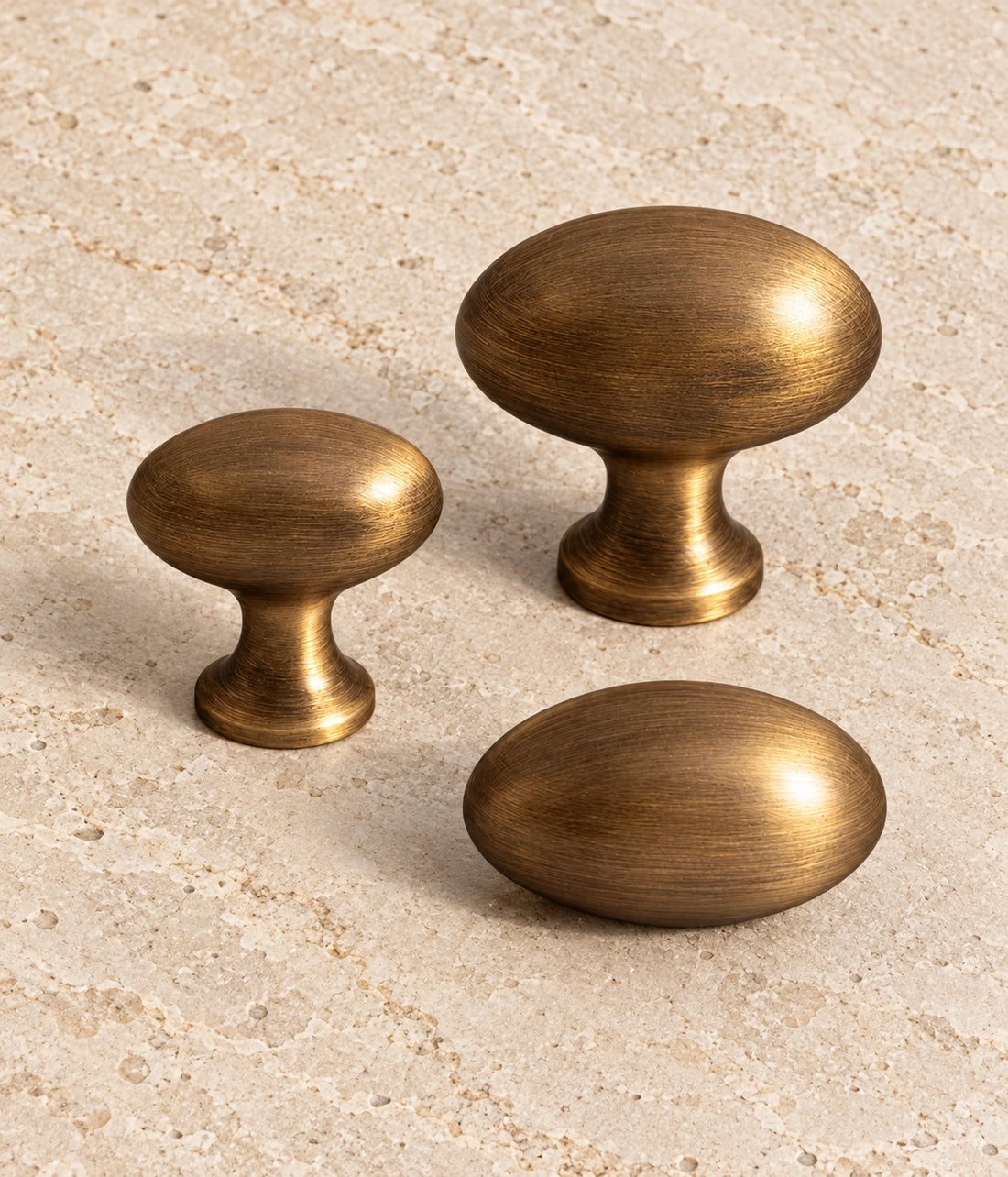 Antique Brass Egg Cabinet Knobs — Pedestal & Stemless on warm limestone