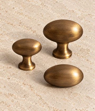 Antique Brass Egg Cabinet Knobs — Pedestal & Stemless on warm limestone