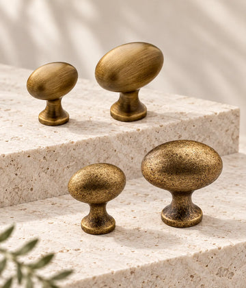 Smooth and distressed antique brass egg cabinet knobs in two sizes on pale stone steps