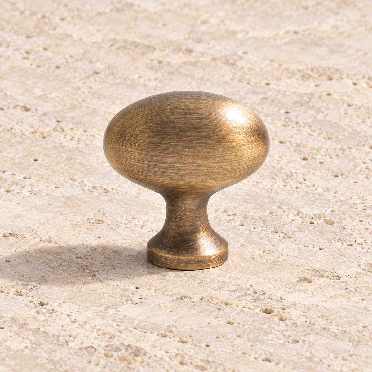 Antique brushed brass egg cabinet knob with oval head on pale limestone