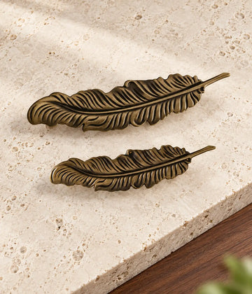 Two antique brass feather cabinet pulls arranged diagonally on warm limestone