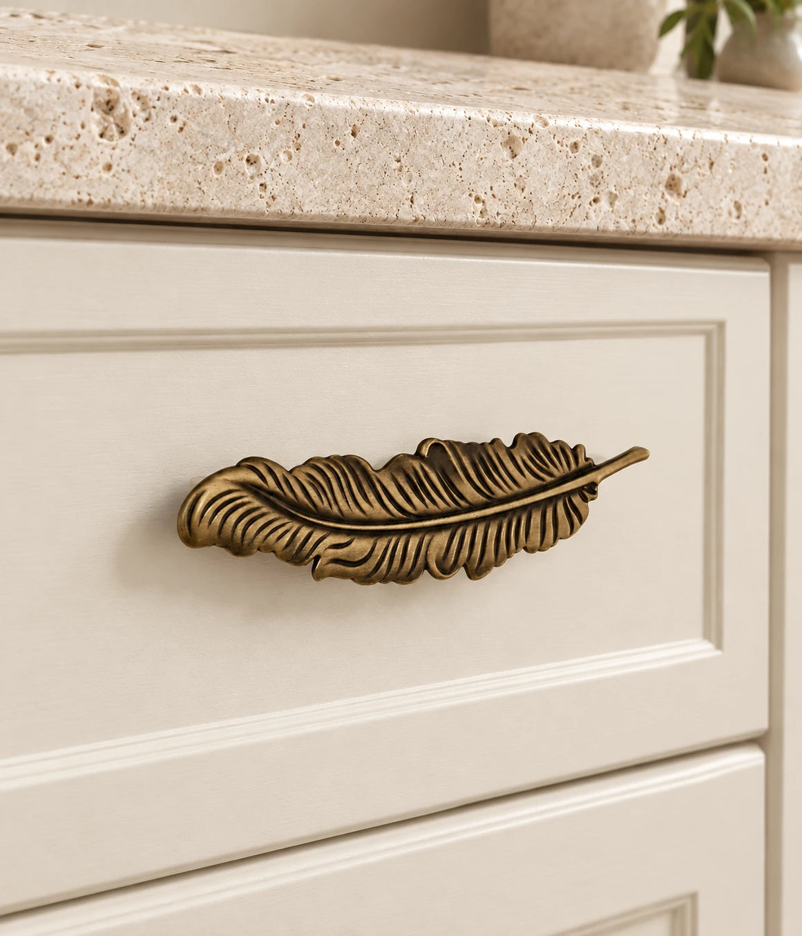 Antique Brass Feather Cabinet Pulls installed on an ivory cabinet drawer
