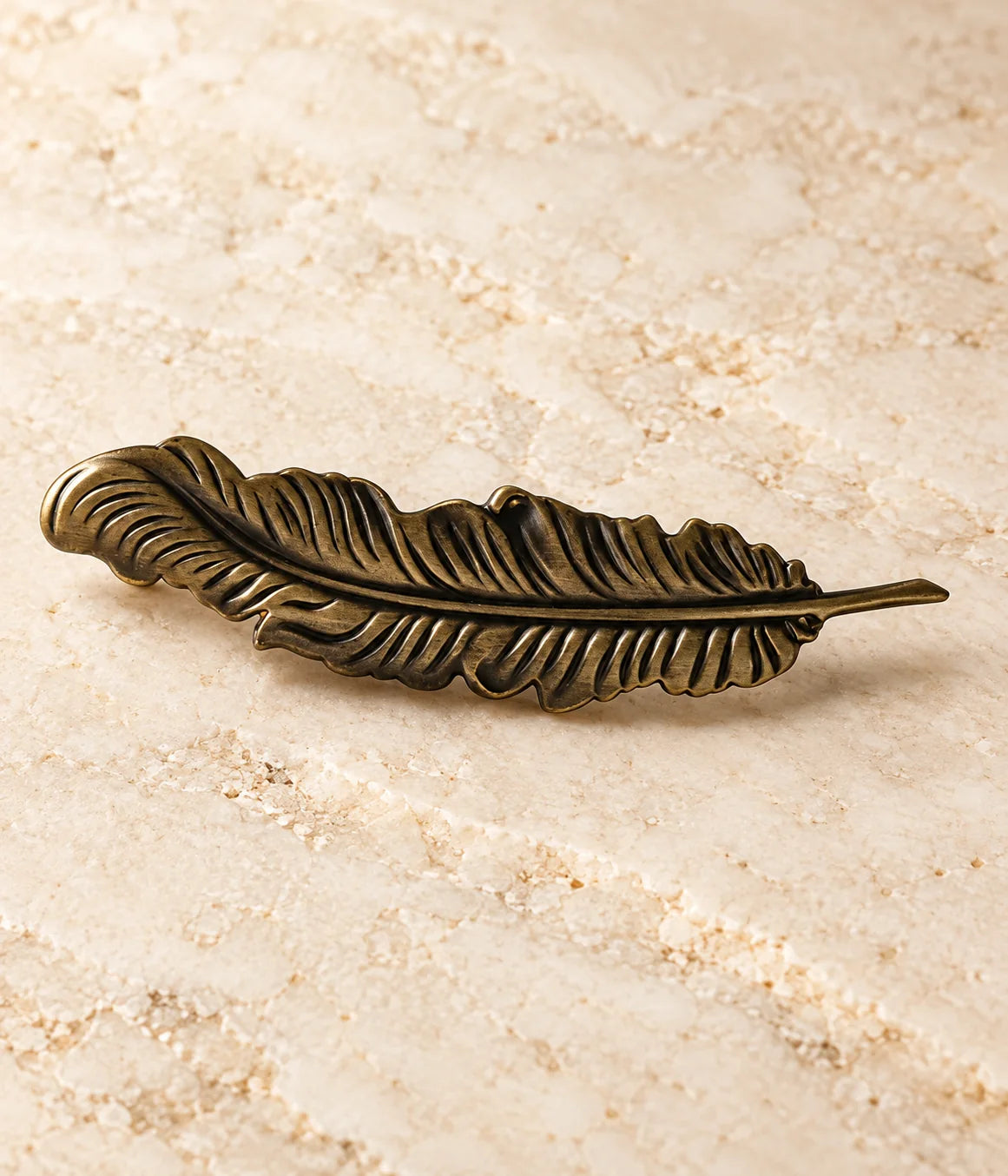 Close view of curved feather spine and detailed antique brass cabinet pull texture