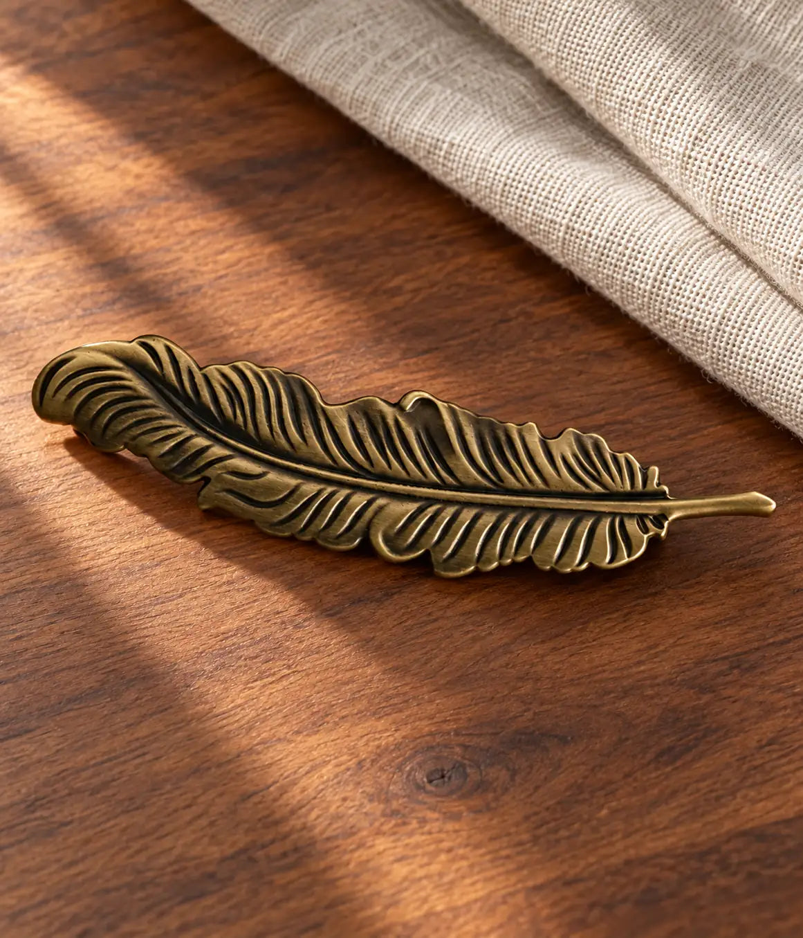 Antique brass feather cabinet pull displayed on walnut wood with neutral linen