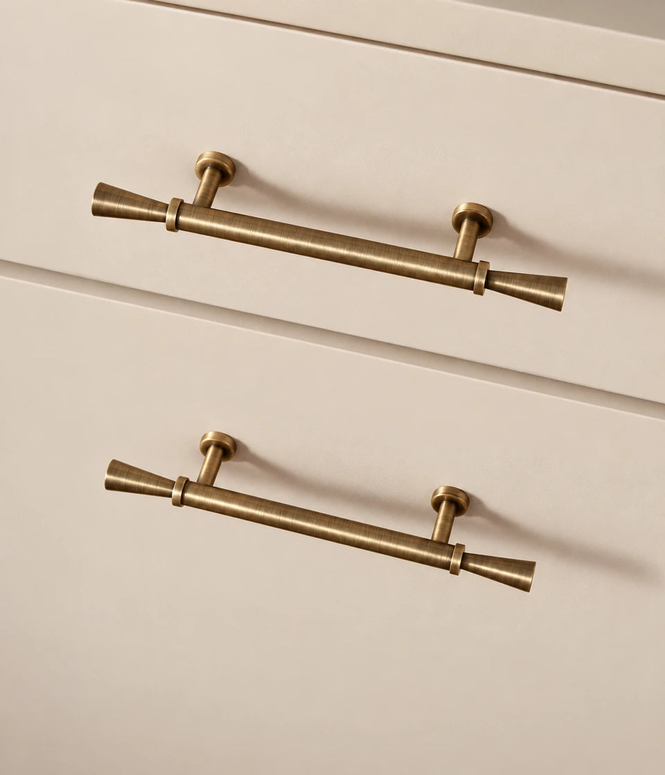 Antique brass flared cabinet pulls installed on cream drawers