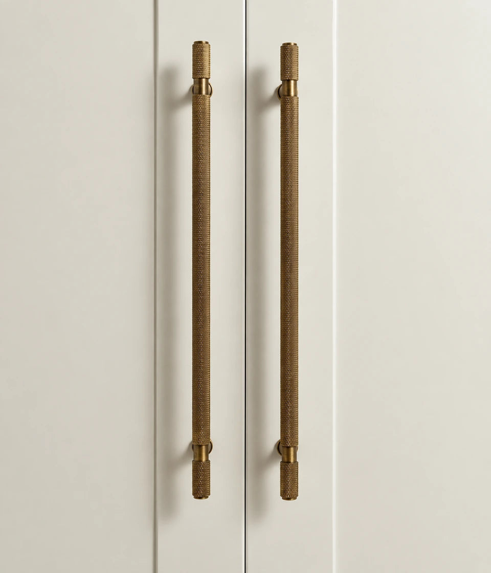 Long antique brass knurled cabinet pulls mounted vertically on cream doors