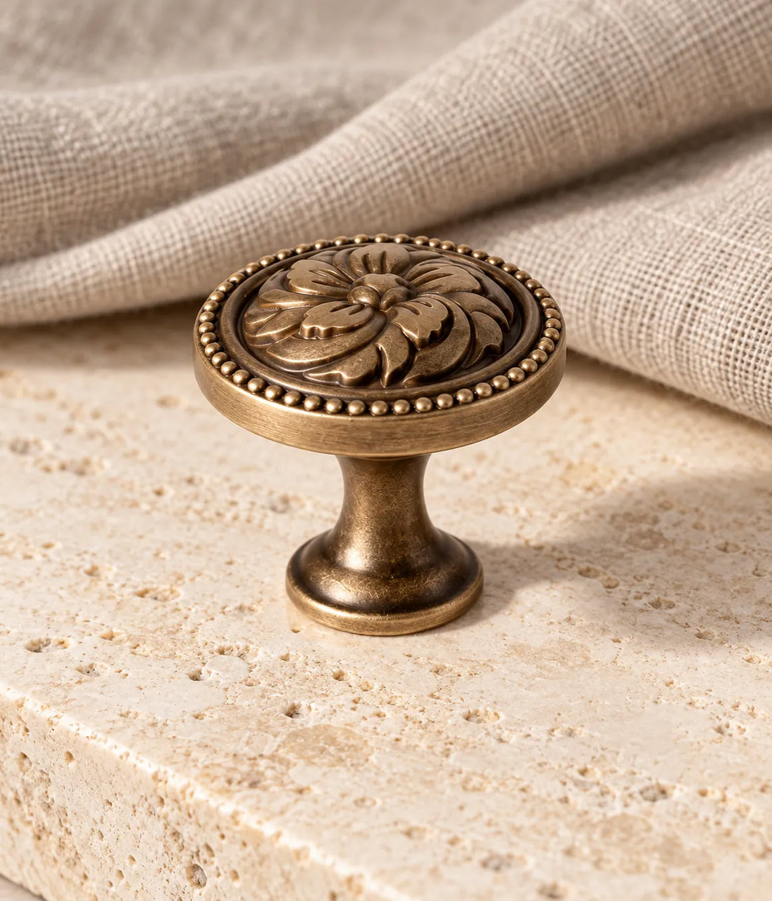 Antique brass floral rosette cabinet knob with beaded rim on warm limestone
