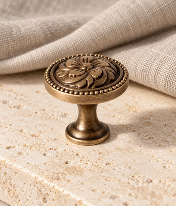 Antique brass floral rosette cabinet knob with beaded rim on warm limestone