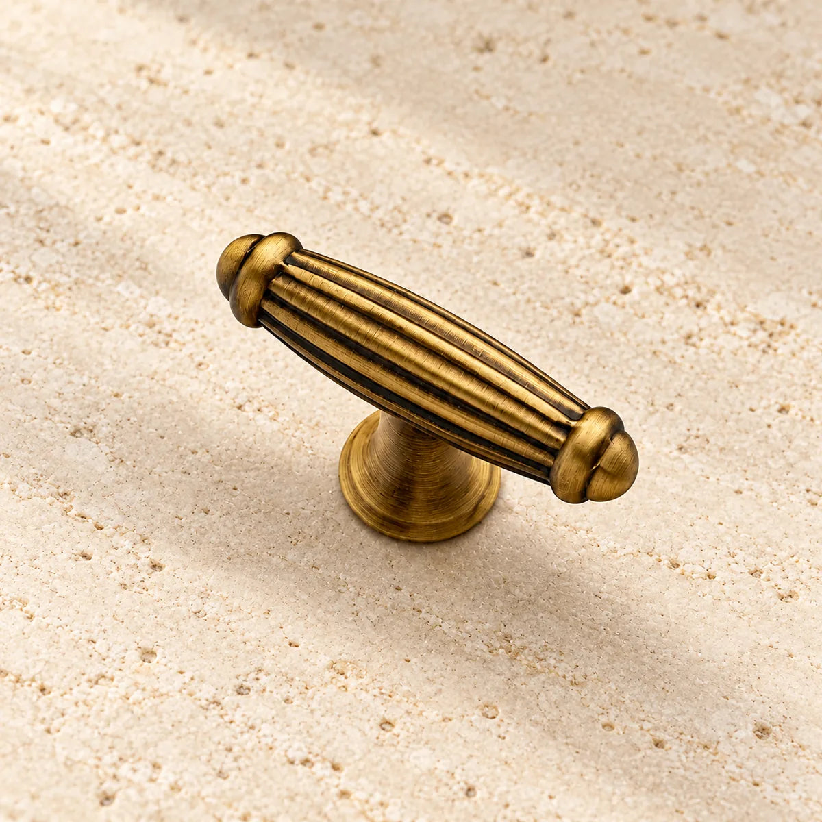 antique brass fluted barrel t bar cabinet knob on pale limestone.