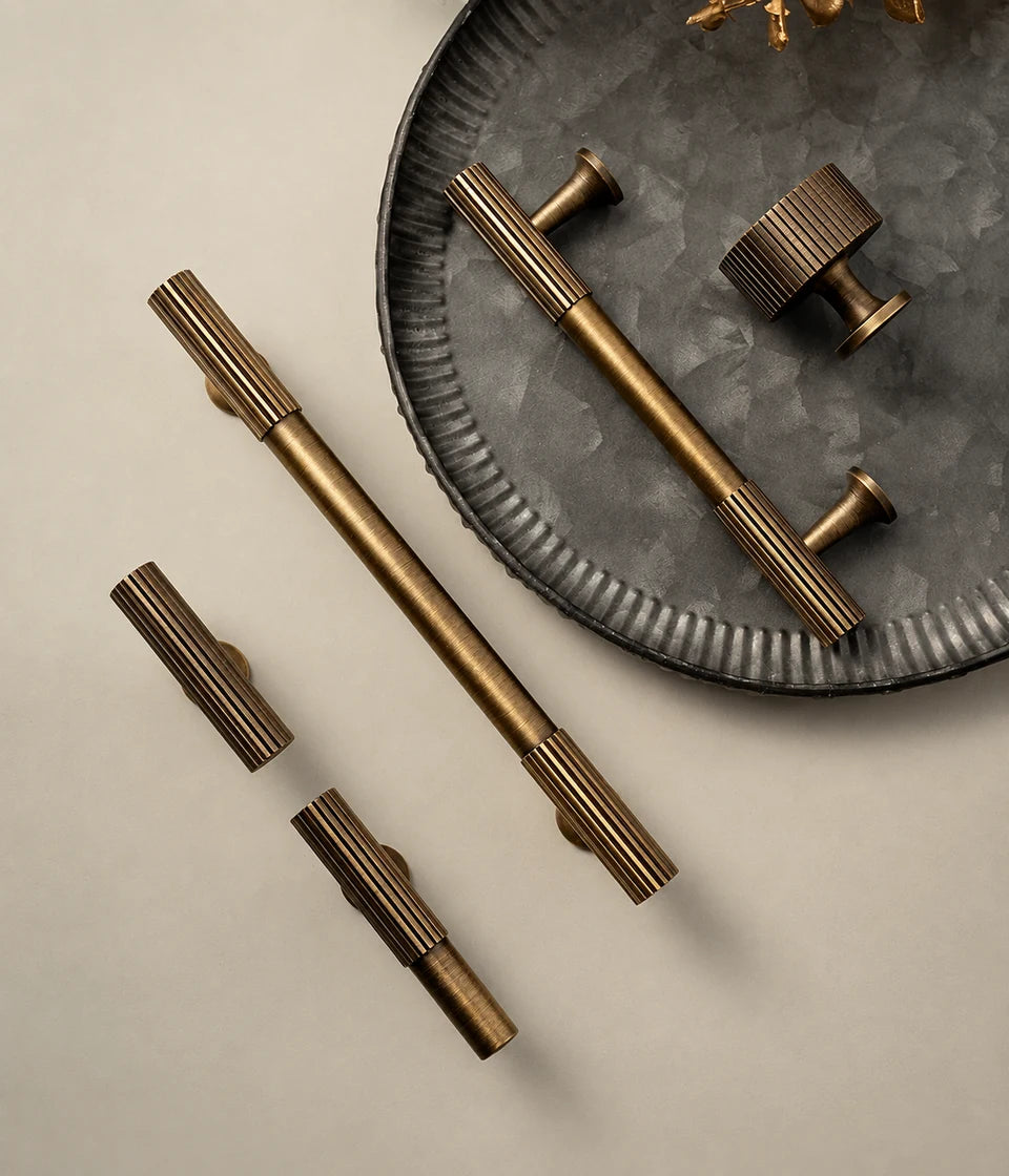 Antique brass fluted end cabinet pulls and drum knob arranged on a dark metal tray