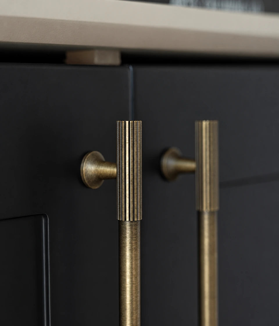 Detail of antique brass fluted end pulls installed on dark cabinet doors