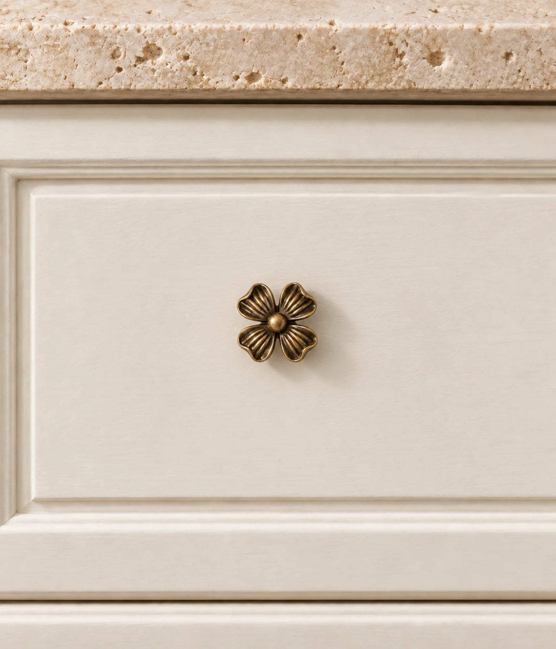 Antique brass four-petal flower cabinet knobs arranged on limestone with linen