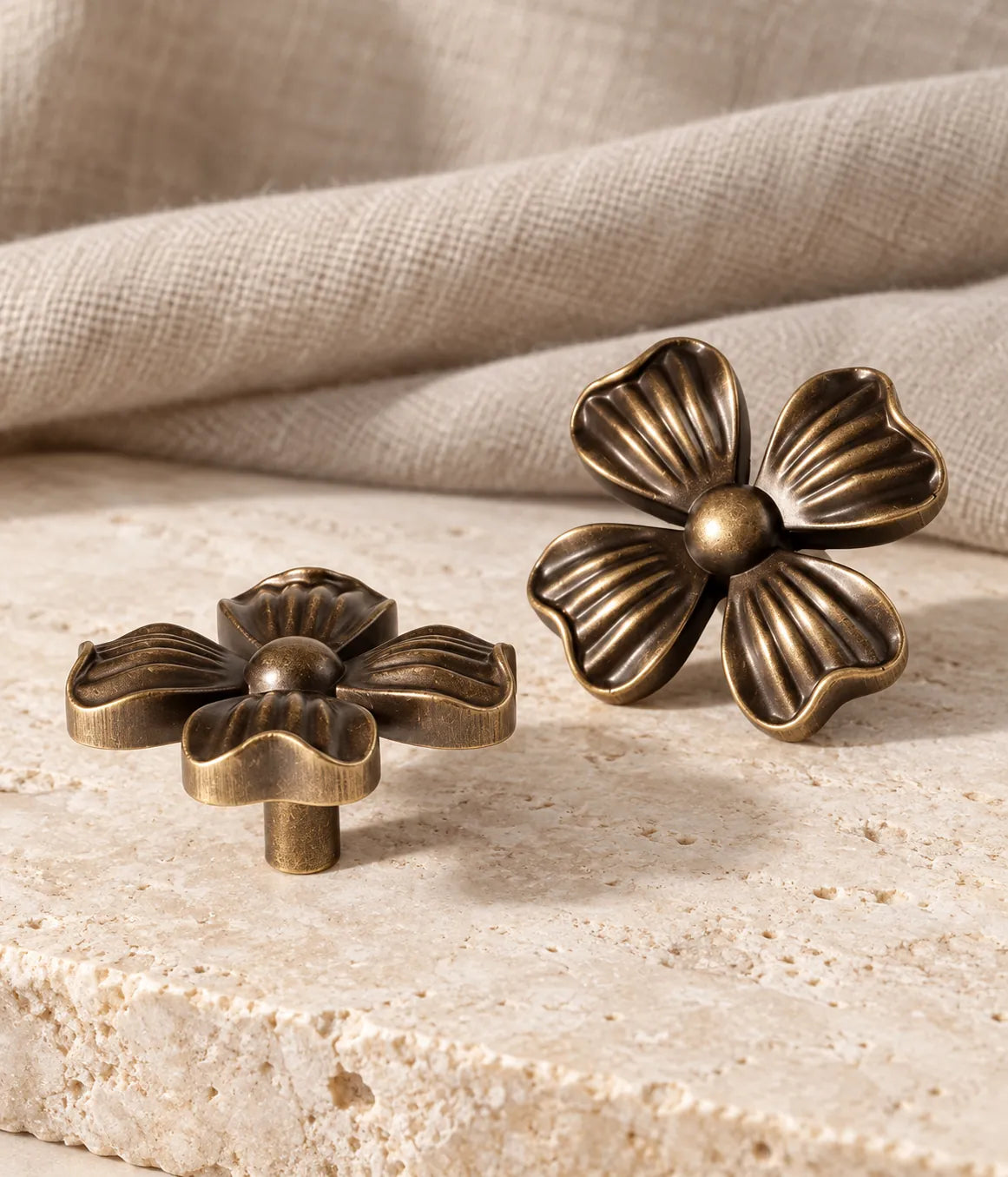 Antique brass four-petal flower cabinet knobs arranged on limestone with linen