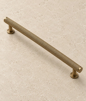 Antique Brass Full Knurled Cabinet Bar Pulls on warm limestone