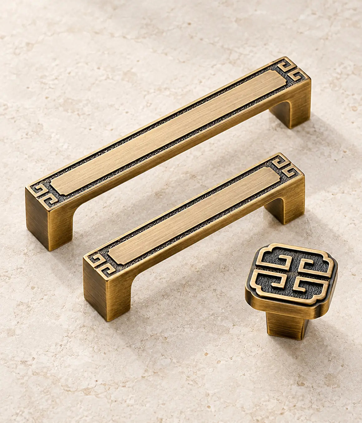 Antique brushed brass geometric cabinet pulls and square knob arranged on limestone