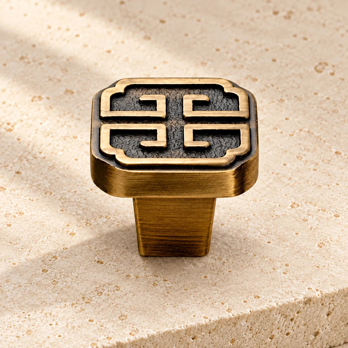 antique brass geometric square cabinet knob on pale limestone.