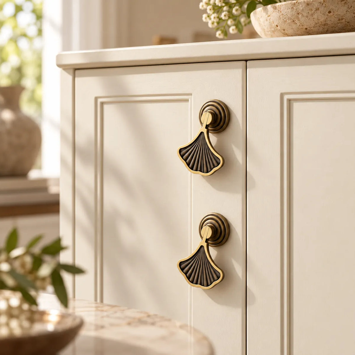 Antique brass ginkgo fan pendant pulls installed on an ivory cabinet