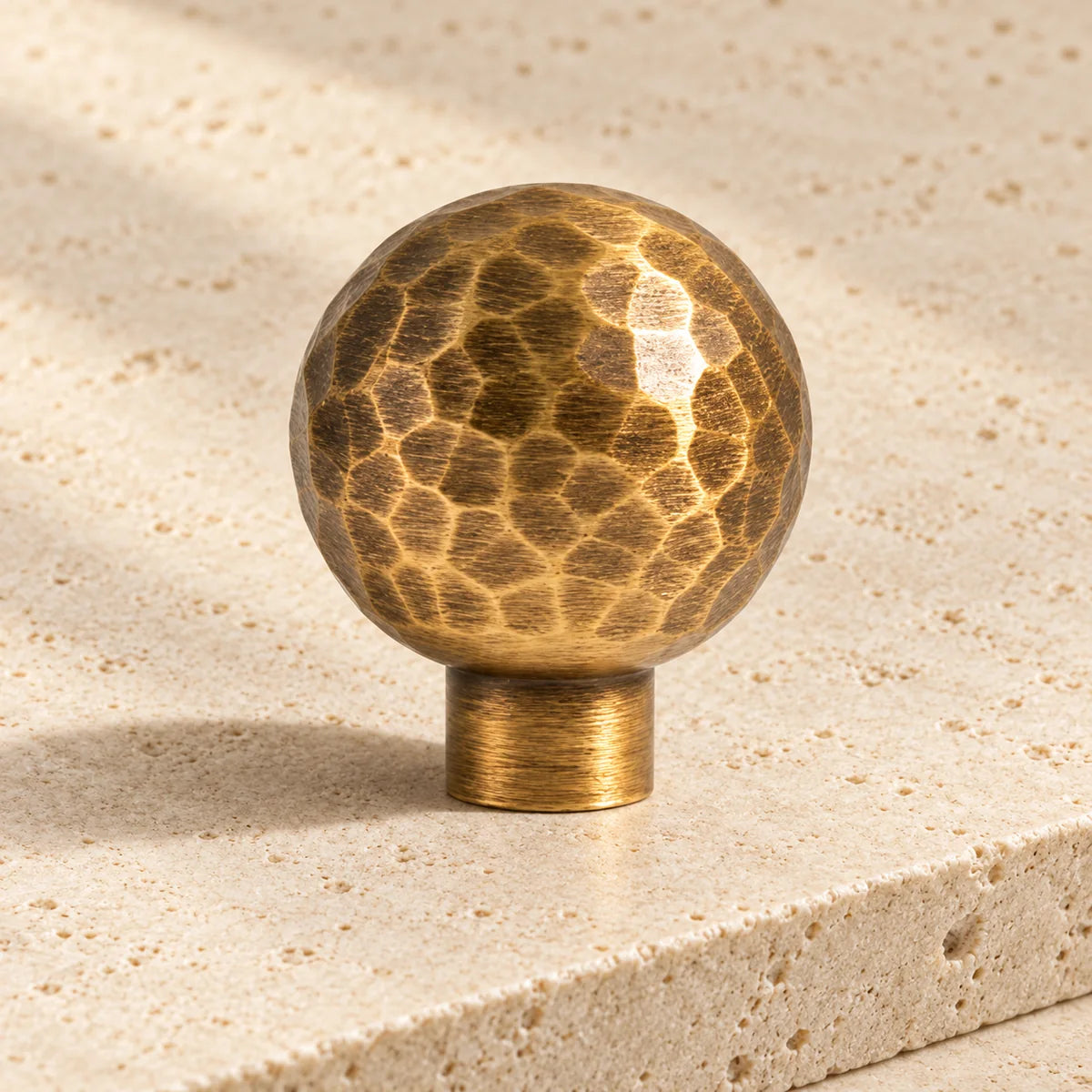 antique brass hammered ball cabinet knob on pale limestone.