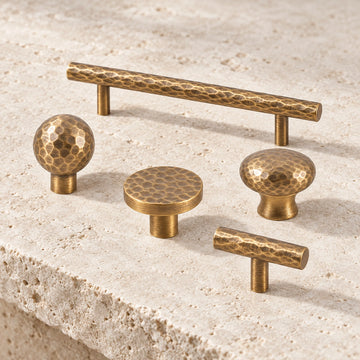 Antique brass hammered bar pulls and ball, flat, domed and T-knobs arranged on limestone
