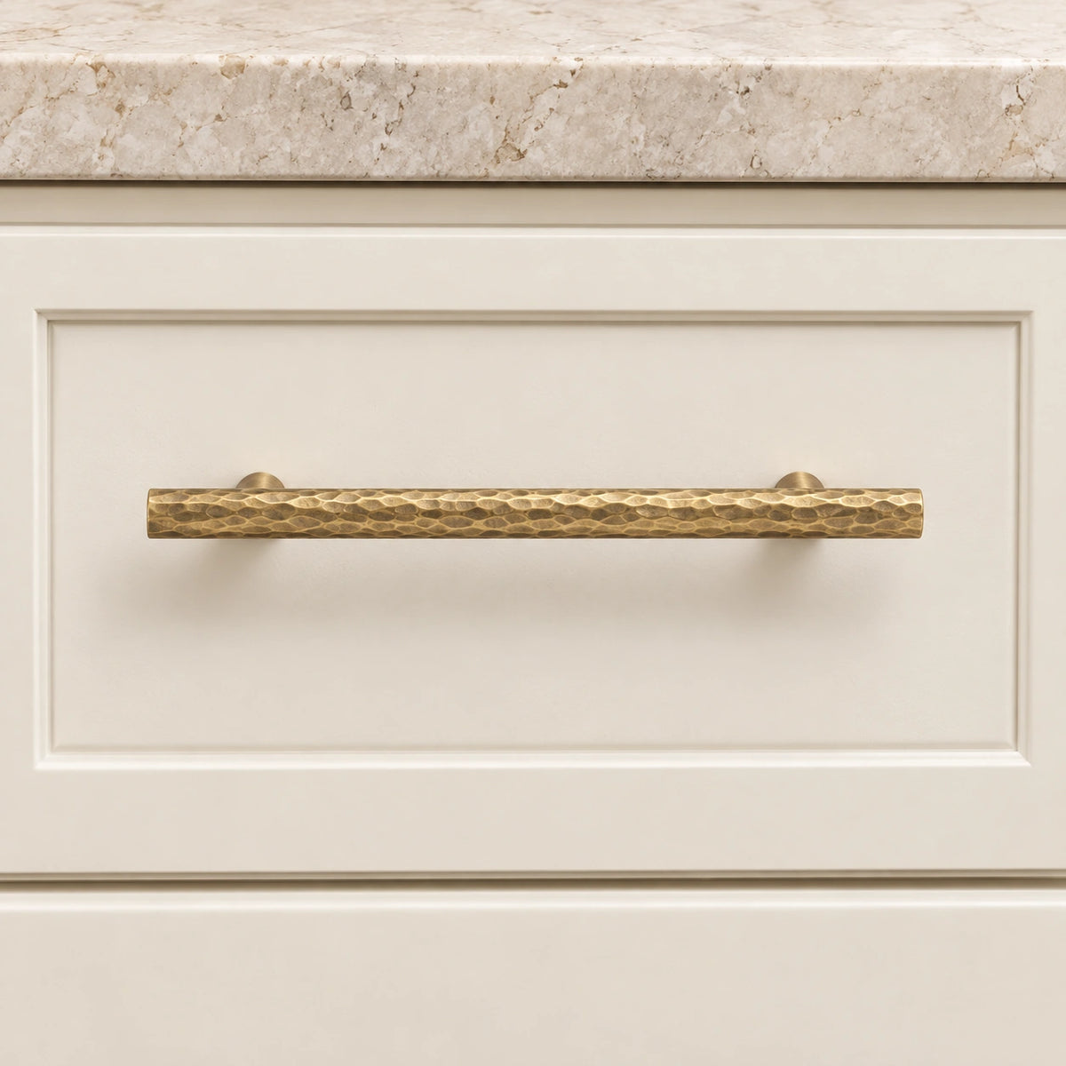 Antique brass hammered bar pull mounted on an ivory cabinet drawer
