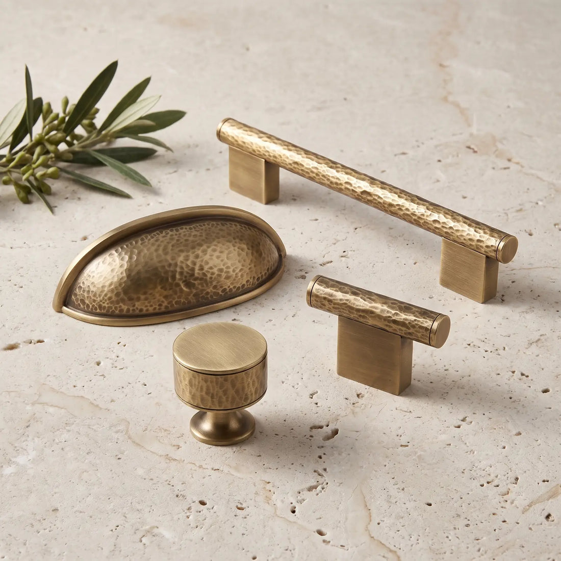 Antique brass hand-hammered cabinet pulls and knobs arranged on pale limestone