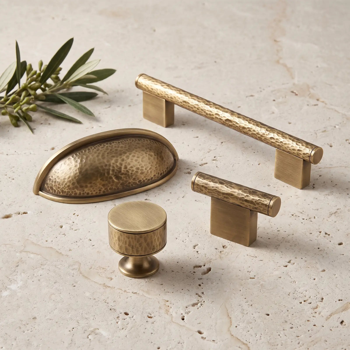 Antique brass hand-hammered cabinet pulls and knobs arranged on pale limestone