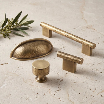 Antique brass hand-hammered cabinet pulls and knobs arranged on pale limestone