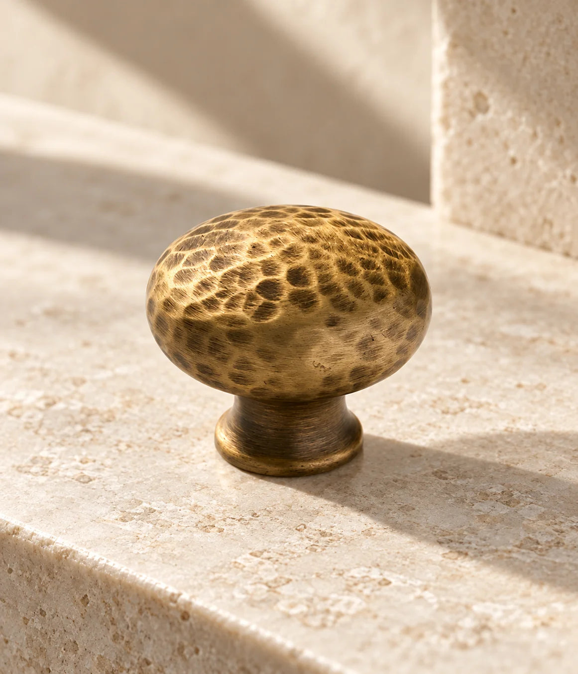 Close view of the hammered round cap and short stem of an antique brass cabinet knob