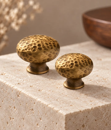 Two antique brass hammered mushroom cabinet knobs on pale limestone