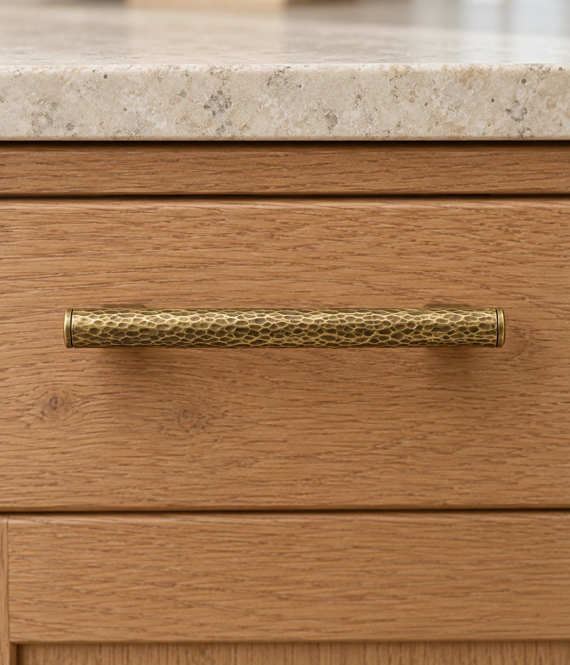 Hand-hammered antique brass cabinet pull installed horizontally on an oak drawer