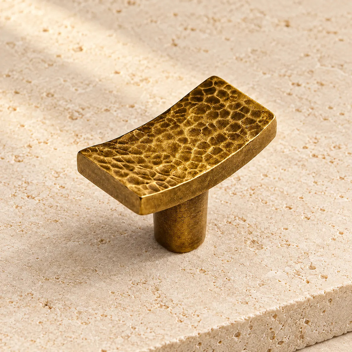 antique brass hammered rectangular cabinet knob on pale limestone.