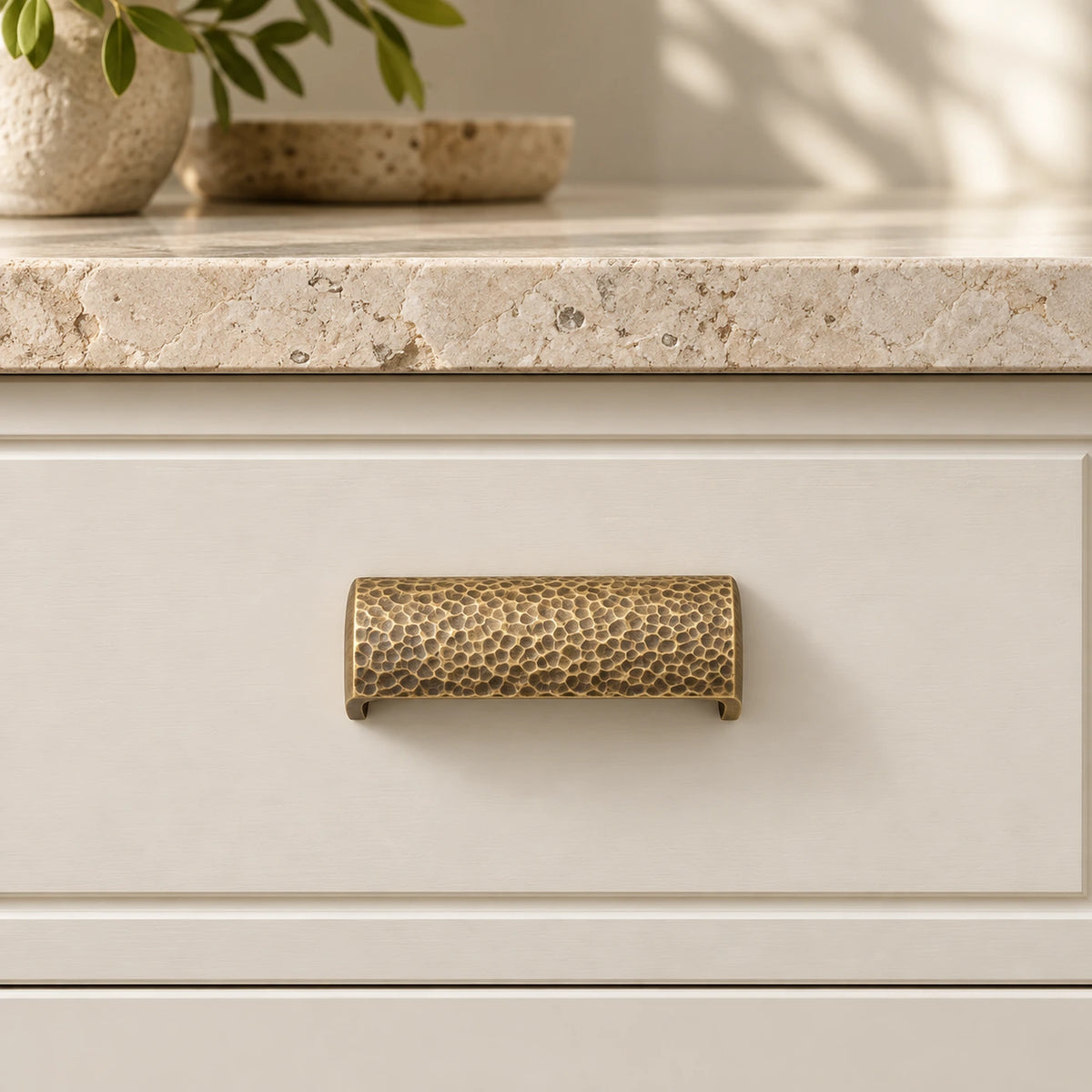 Antique brass hammered semicircle pull installed on an ivory cabinet drawer