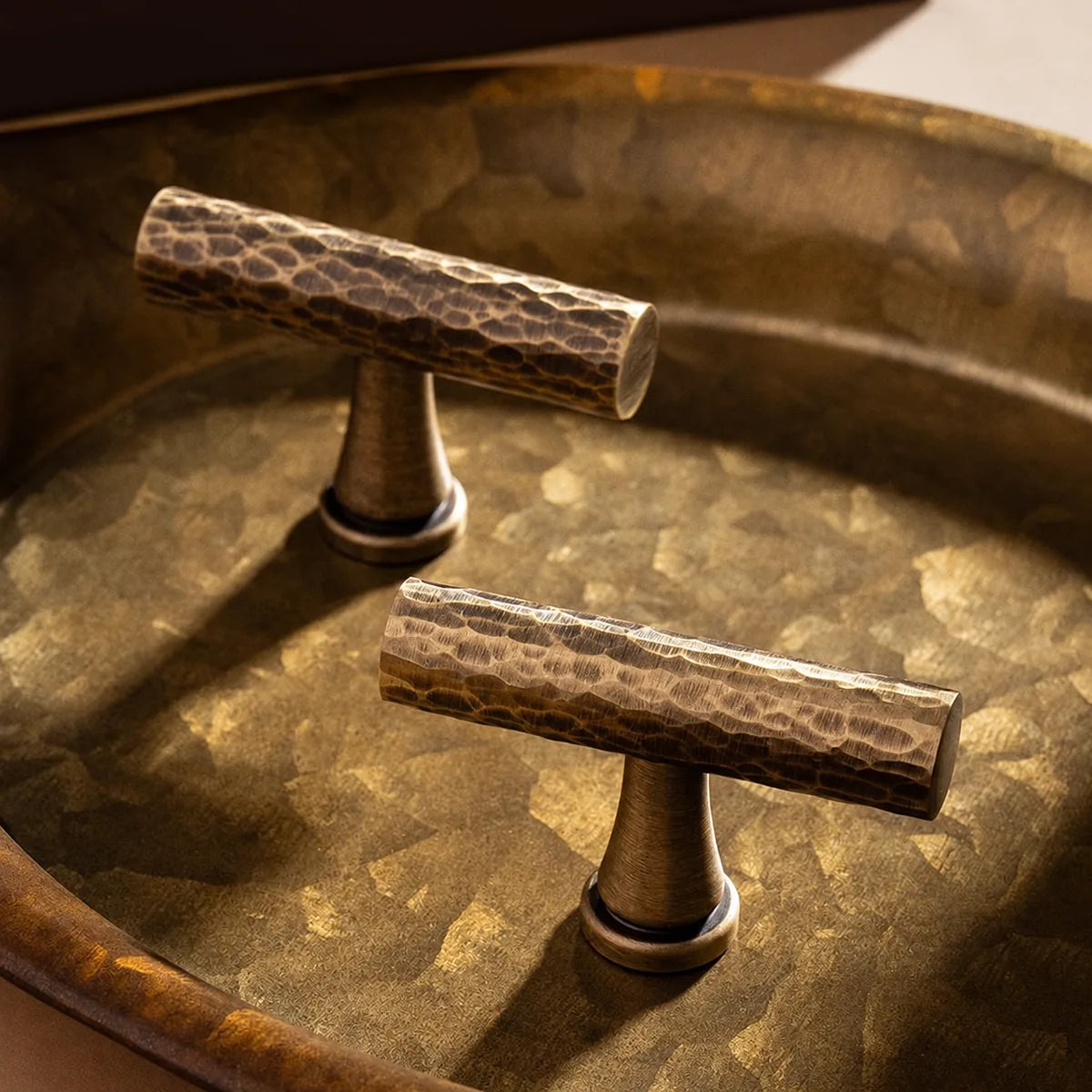 Two hammered antique brass T-knobs on a metal tray