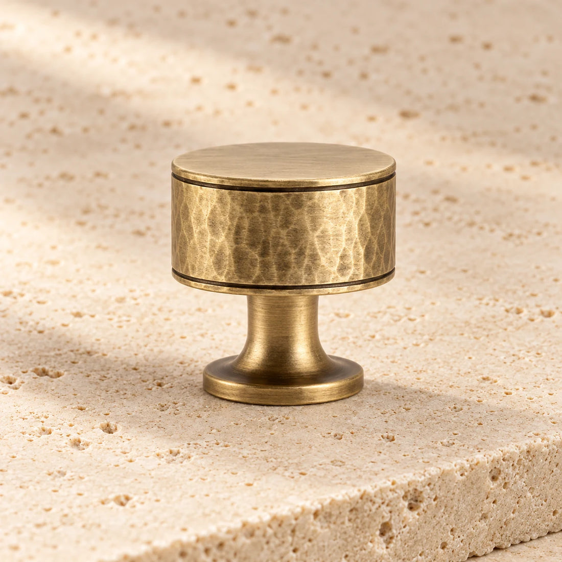 antique brass hand hammered round cabinet knob on pale limestone.