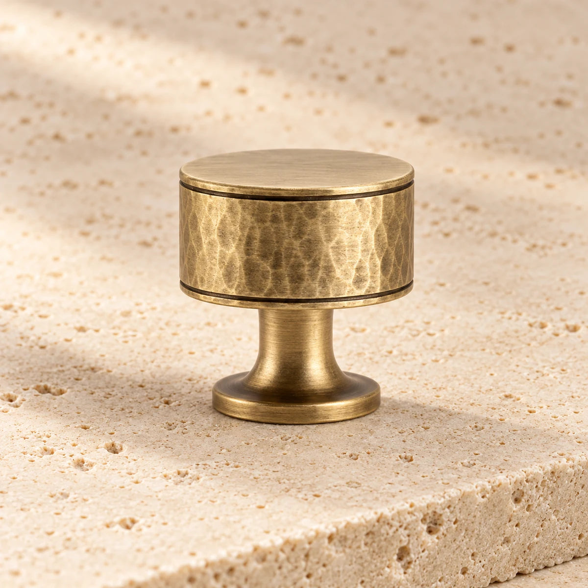 antique brass hand hammered round cabinet knob on pale limestone.