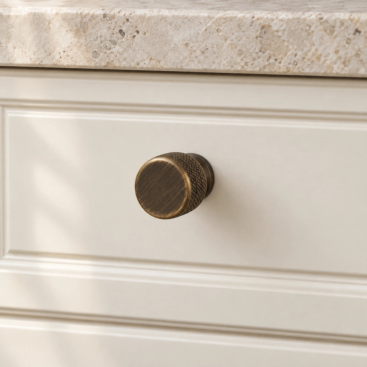 Antique brass cabinet knob mounted on an ivory drawer