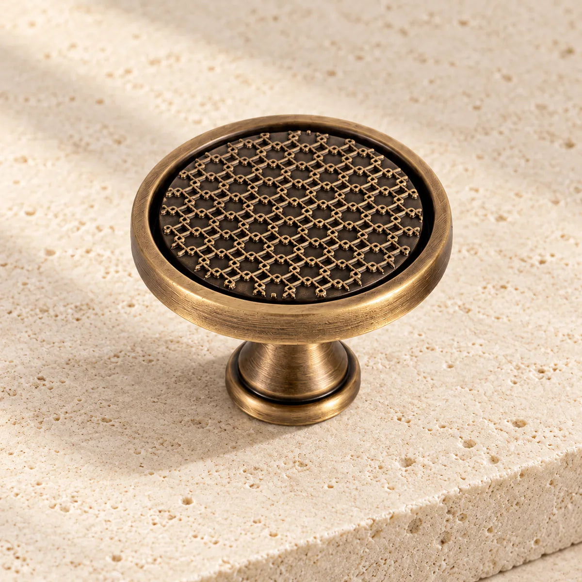 antique brass lattice round cabinet knob on pale limestone.