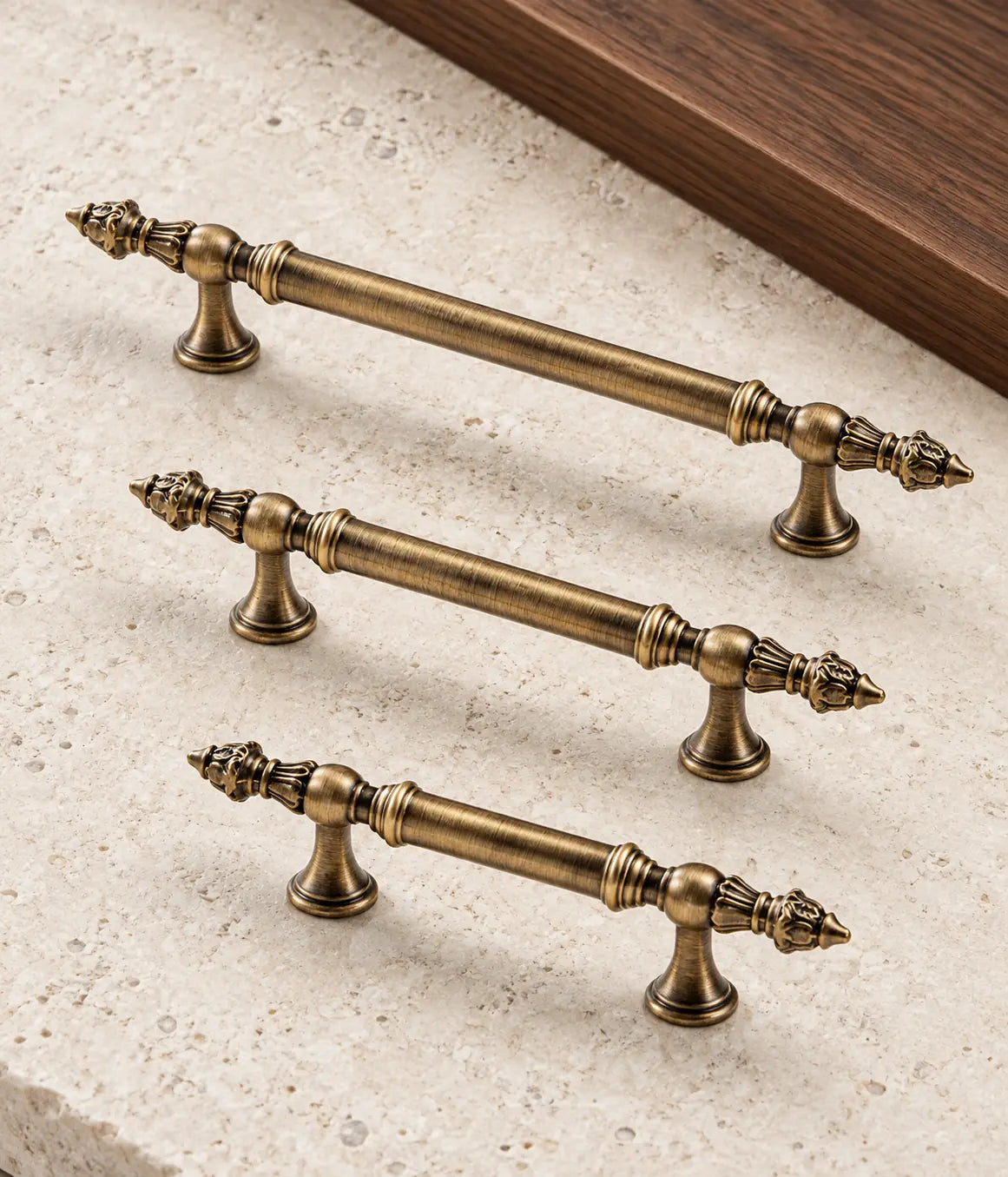 Three antique brass leaf-finial cabinet pulls arranged on pale limestone