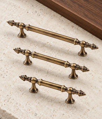 Three antique brass leaf-finial cabinet pulls arranged on pale limestone