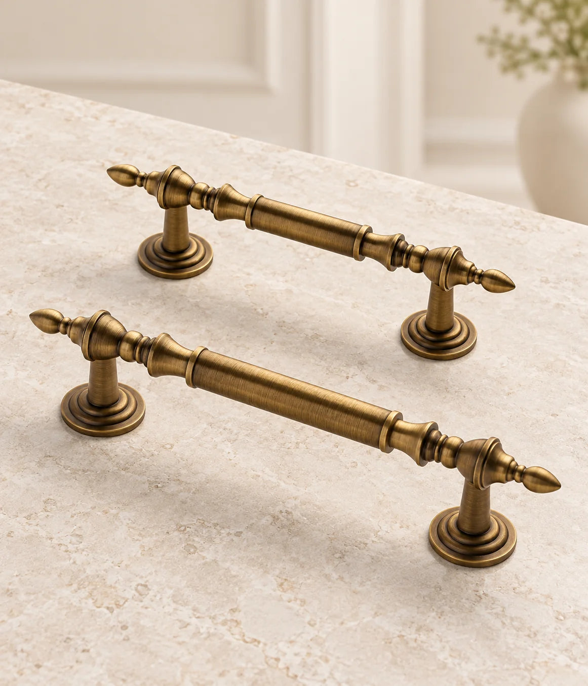 Antique brass leaf-tip cabinet pulls in two sizes arranged on pale limestone