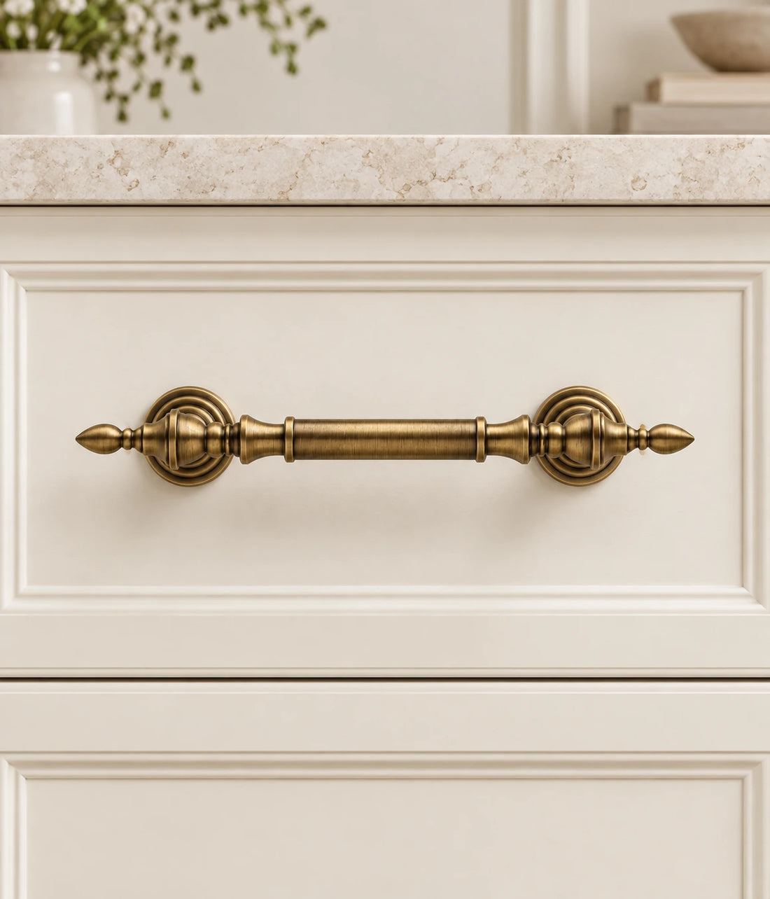 Antique brass leaf-tip cabinet pulls in two sizes arranged on pale limestone
