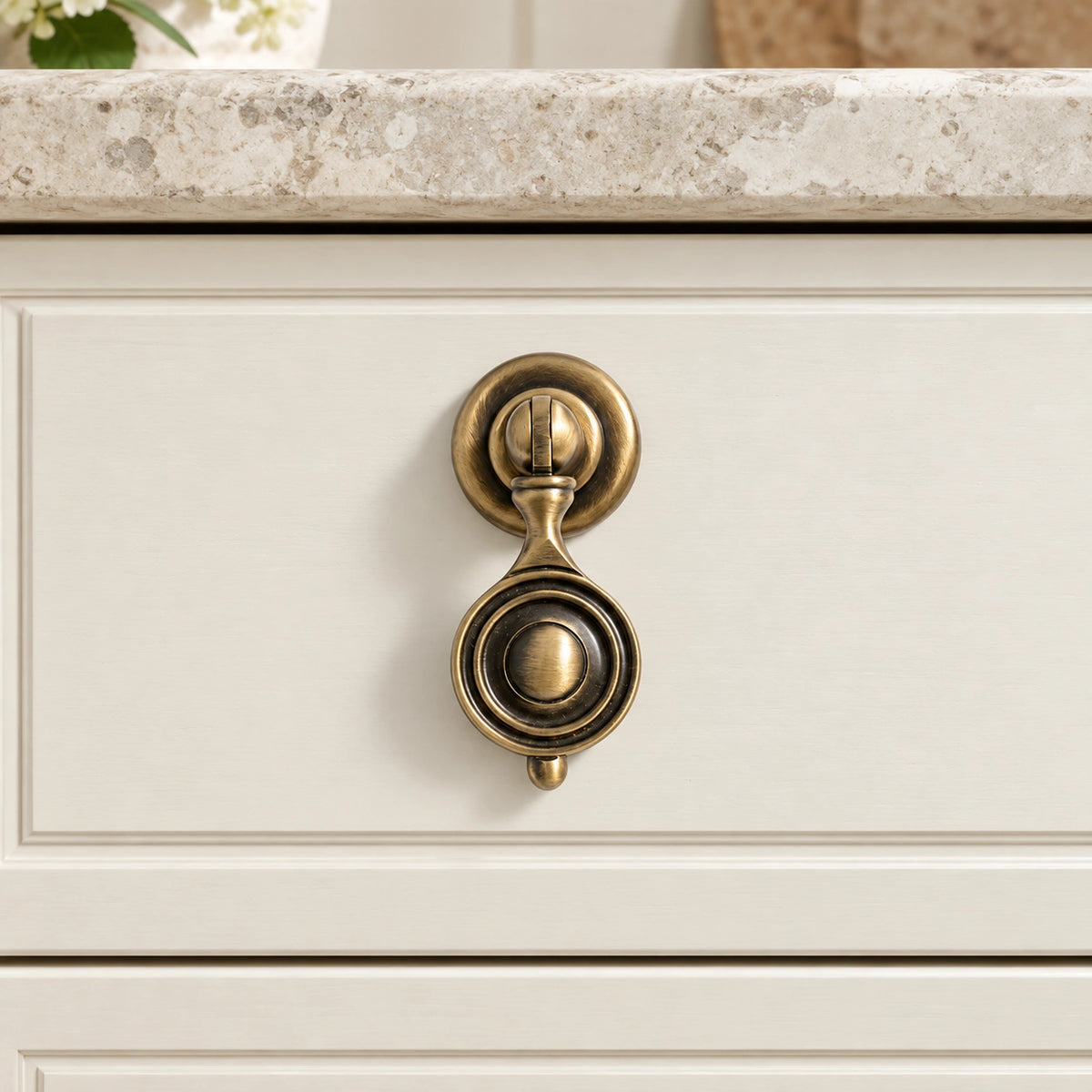 Antique brass medallion drop pull mounted on an ivory cabinet drawer