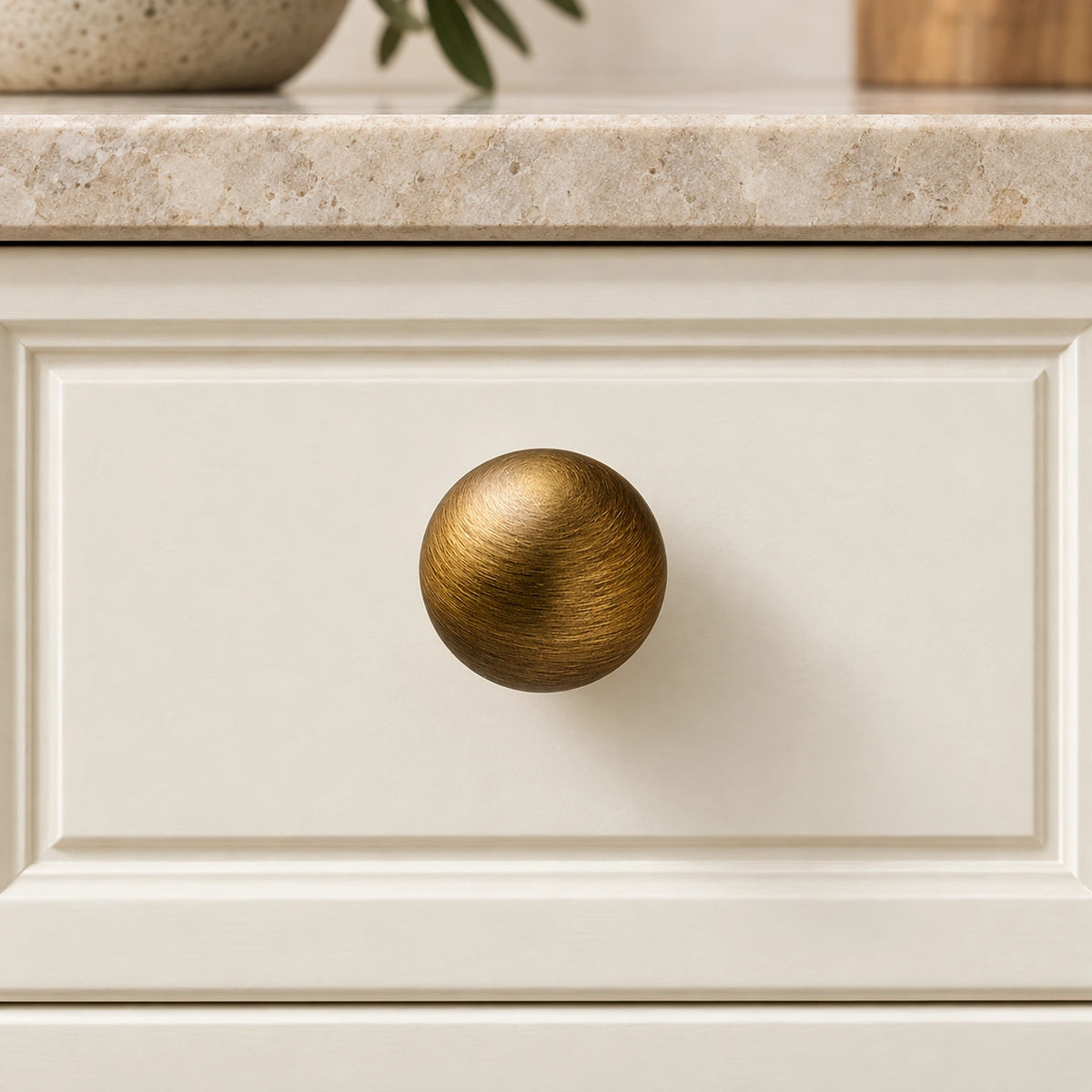 Antique brass ball knob mounted on an ivory drawer beneath a limestone counter