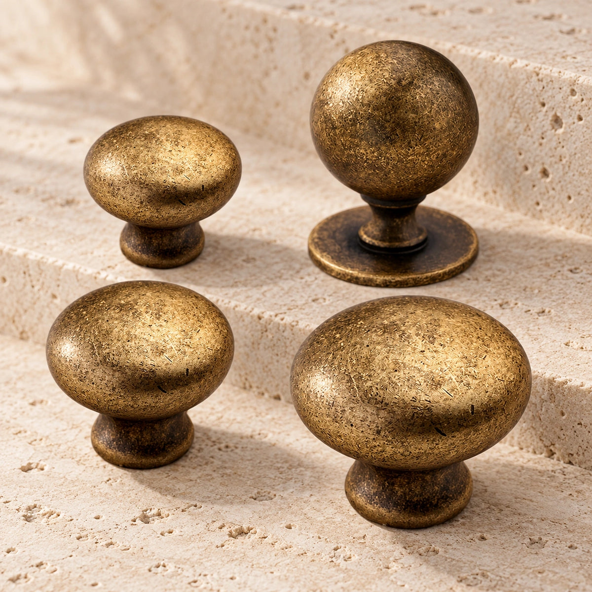 Mottled antique brass mushroom and ball cabinet knobs arranged on pale limestone