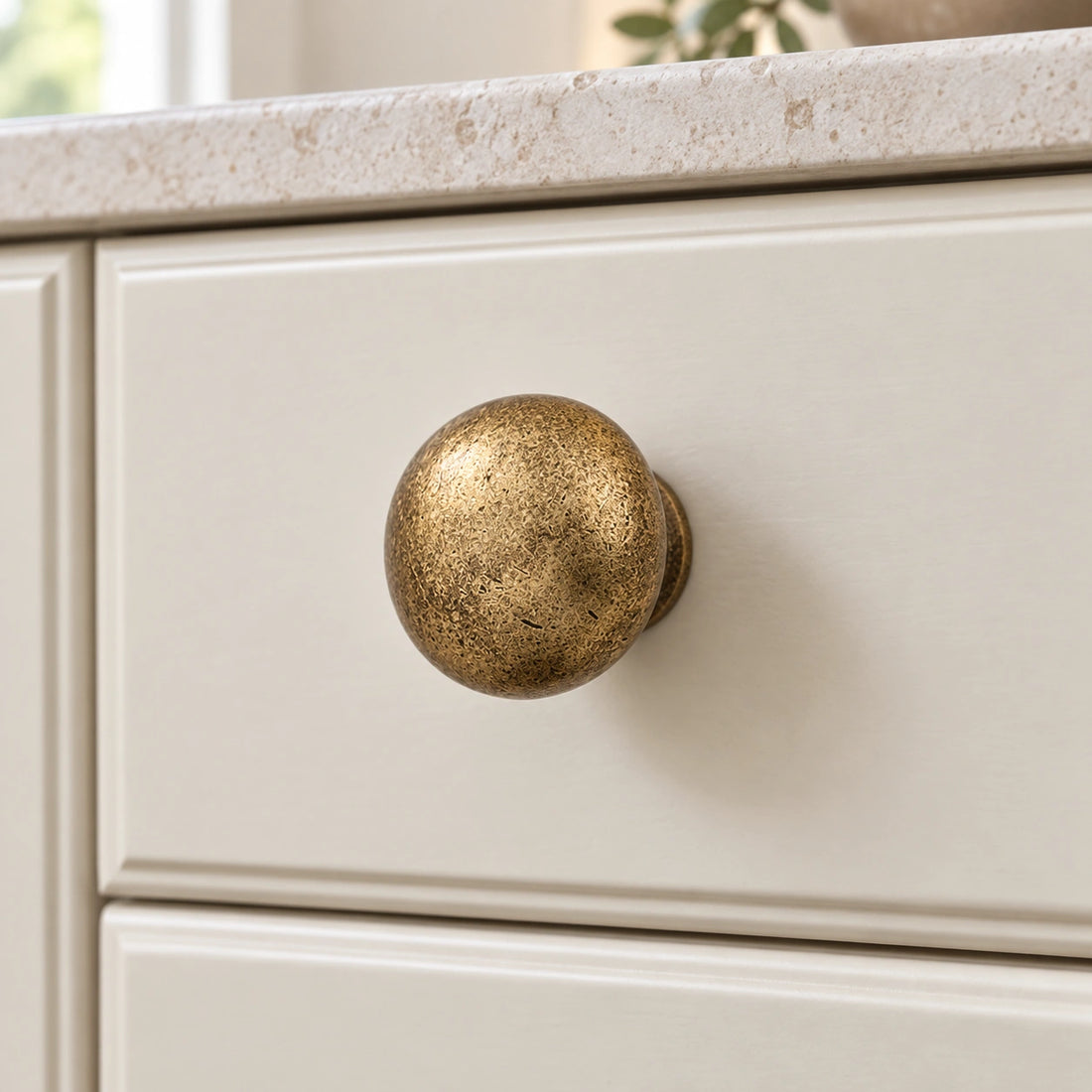 Mottled antique brass mushroom and ball cabinet knobs arranged on pale limestone