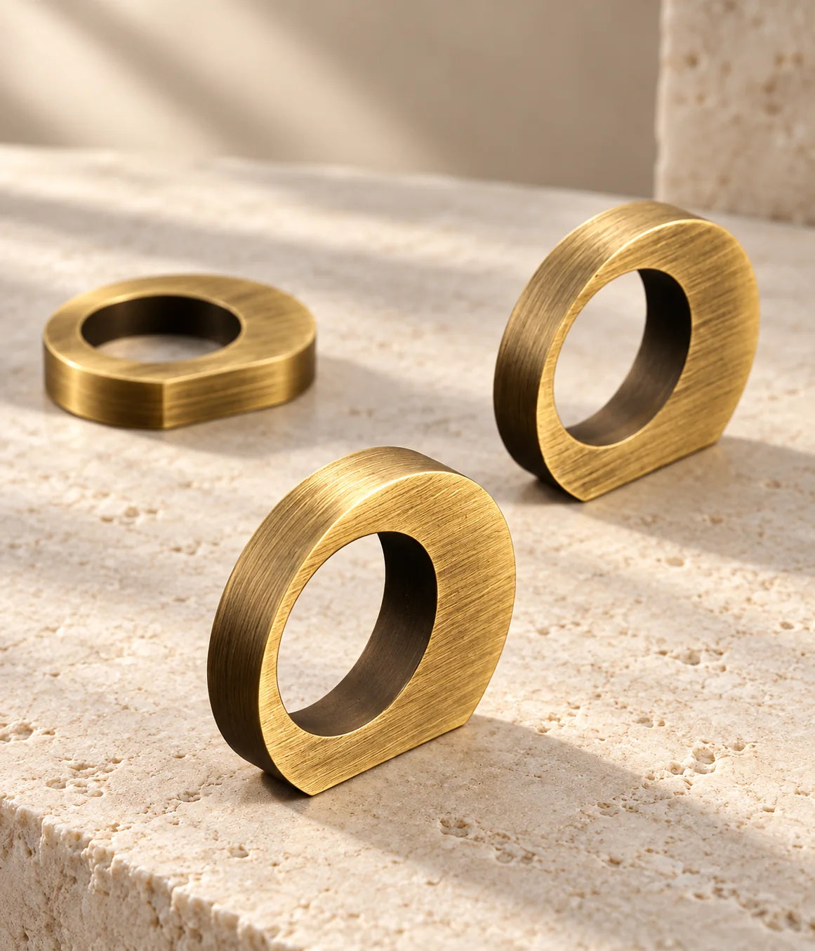 Antique brass offset ring cabinet pulls arranged on pale limestone