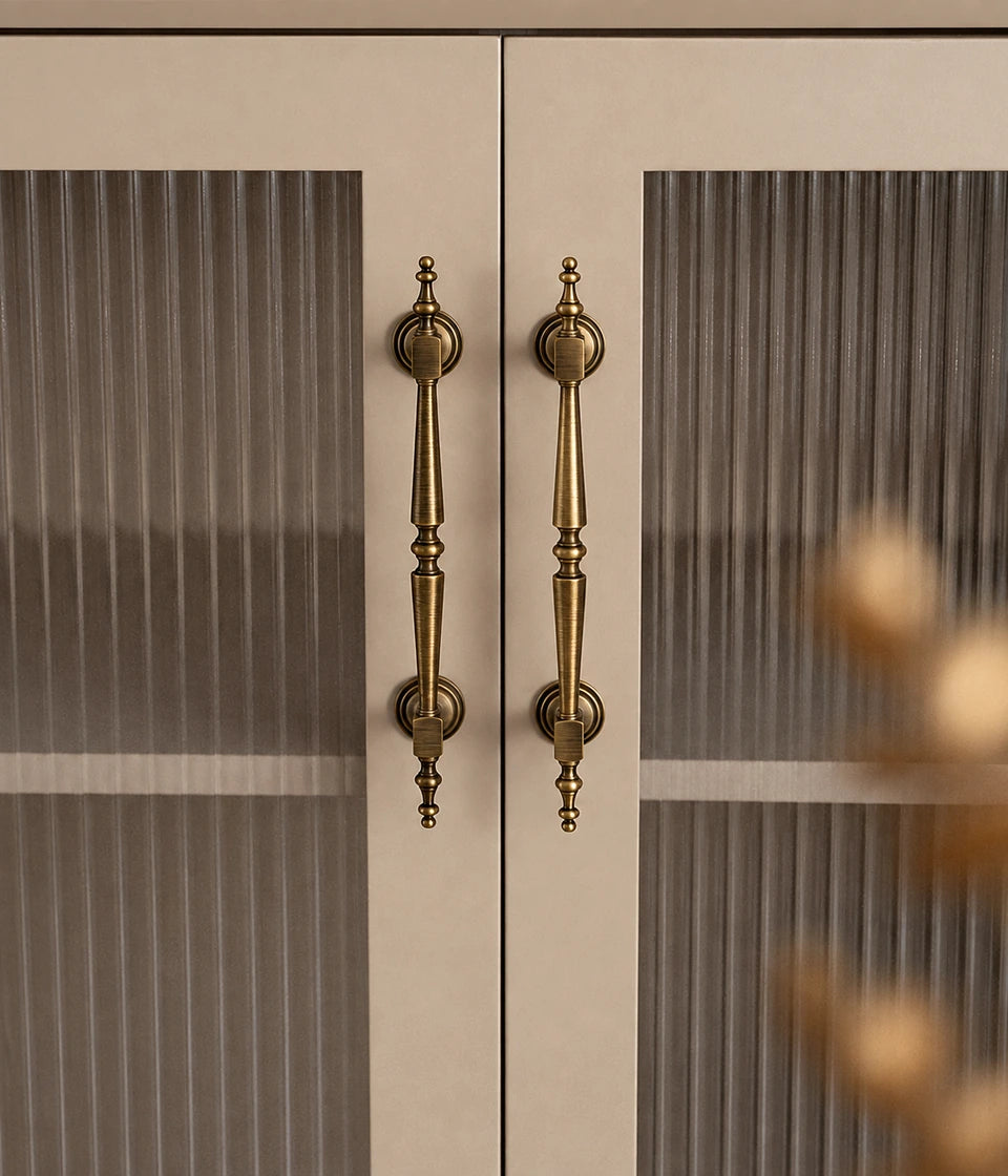 Ornate antique brass cabinet pulls installed vertically on glass cabinet doors