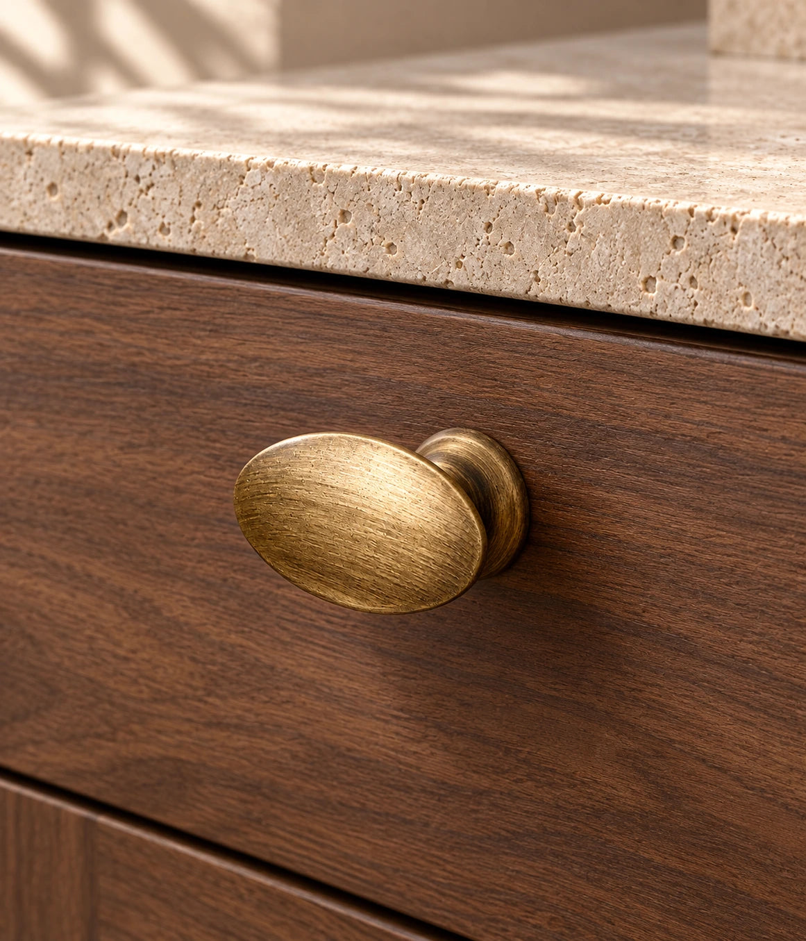 Smooth antique brass oval cabinet knob installed on walnut drawer